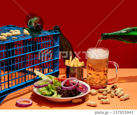 Beer pouring into glass with snacks and fresh salad on bright red background with copy space. Beer pouring into glass with snacks and fresh salad on bright red background with copy space. 137855041