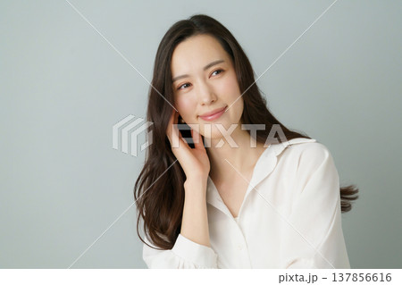 グレーバックの頬に手を当てる白いシャツを着た若い日本人女性のポートレート 137856616