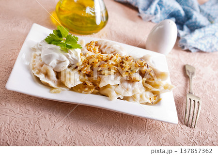 A plate with boiled dough vareniki with potato filling and fried onions. 137857362