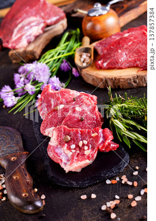 Seasoned raw beef steak with sea salt, cracked pepper, rosemary sprigs, and garlic cloves on black slate. Seasoned raw beef steak with sea salt, cracked pepper, rosemary sprigs, and garlic cloves on black slate. 137857384