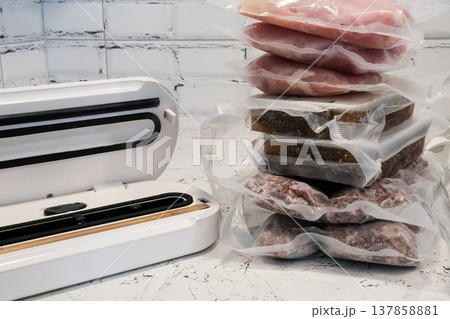 Home vacuum packer for food storage and freezing, canning products. Portions of vacuum-packed raw chicken breast, minced meat and frozen meat broth for cooking and souping. 137858881