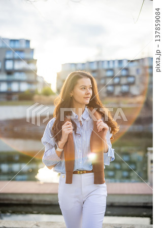 Elegant young woman in old money style walking by riverside near Prague pier during golden hour. Quiet luxury aesthetic and confident European lifestyle concept. Elegant young woman in old money style walking by riverside near Prague pier during golden hour. Quiet luxury aesthetic and confident European lifestyle concept. 137859084