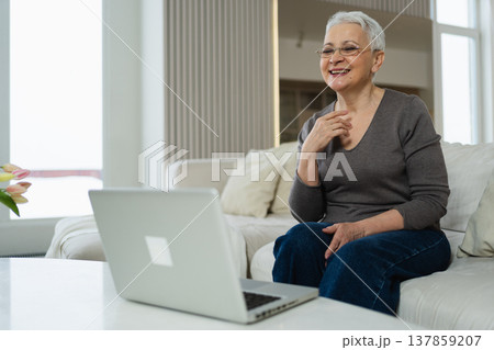 Happy middle aged senior woman siting with laptop talking on video call with friends family. Laughing mature old senior grandmother having fun talking speaking with grown up children online 137859207
