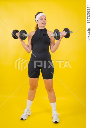 Woman exercising arms with dumbbells on yellow background 137859324