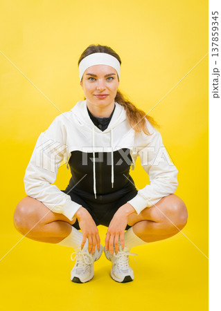 Sporty woman squatting posing on yellow background 137859345
