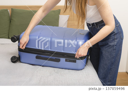 Woman zipping a blue hard shell suitcase on a bed while finishing packing at home. Close-up travel Woman zipping a blue hard shell suitcase on a bed while finishing packing at home. Close-up travel 137859496
