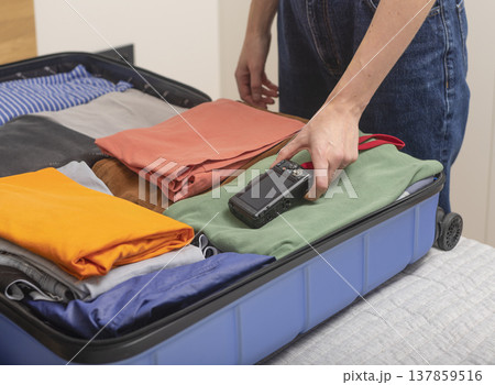 Camera and travel essentials lie on the bed as packing begins at home. Cropped female hands place Camera and travel essentials lie on the bed as packing begins at home. Cropped female hands place 137859516