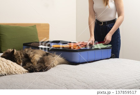 Camera gear and clothes pile up beside an open suitcase on the bed. A cute cat sleeps nearby while Camera gear and clothes pile up beside an open suitcase on the bed. A cute cat sleeps nearby while 137859517