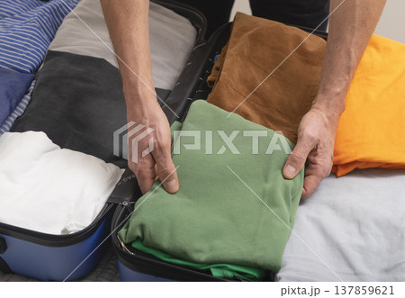 Hands placing neatly folded clothes into an open suitcase during packing at home. Close-up travel Hands placing neatly folded clothes into an open suitcase during packing at home. Close-up travel 137859621