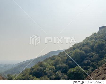 Hazy mountain landscape with layered green hills fading into the distance under a pale sky. Calm Hazy mountain landscape with layered green hills fading into the distance under a pale sky. Calm 137859622