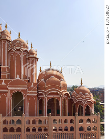 Iconic pink sandstone facade of Hawa Mahal with ornate arches and domed pavilions against a clear Iconic pink sandstone facade of Hawa Mahal with ornate arches and domed pavilions against a clear 137859627