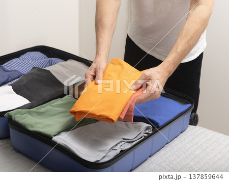 Open luggage on the bed fills as clothes get folded for a trip. Cropped hands place personal Open luggage on the bed fills as clothes get folded for a trip. Cropped hands place personal 137859644