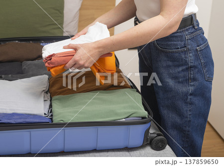 Open suitcase on the bed as clothing gets folded for a weekend escape. Cropped female hands place Open suitcase on the bed as clothing gets folded for a weekend escape. Cropped female hands place 137859650