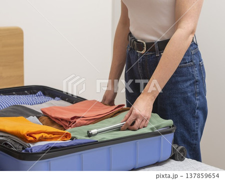 Open suitcase on the bed receives a personal hygiene case with toothbrush during packing. Cropped Open suitcase on the bed receives a personal hygiene case with toothbrush during packing. Cropped 137859654