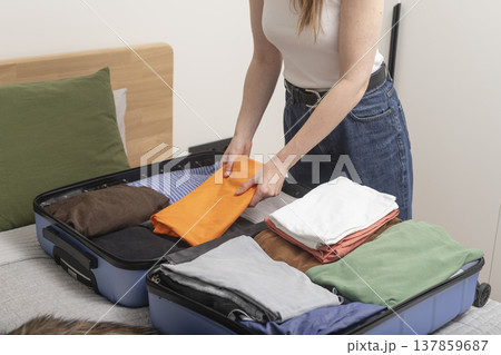 ropped female hands fold clothes and stack personal essentials into baggage for travel abroad. ropped female hands fold clothes and stack personal essentials into baggage for travel abroad. 137859687