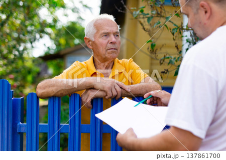 Senior man communicating with insurance company representative while standing at fence of his country house Senior man communicating with insurance company representative while standing at fence of his country house 137861700