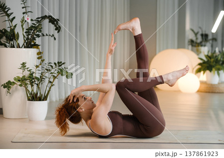 Yoga practice in a modern studio with a woman performing an exercise on a mat during the daytime surrounded by plants and soft lighting 137861923