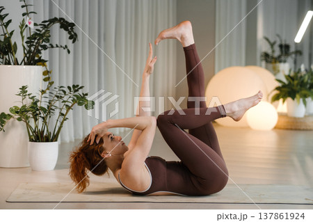 Yoga practice in a modern studio with a woman performing an exercise on a mat during the daytime surrounded by plants and soft lighting 137861924
