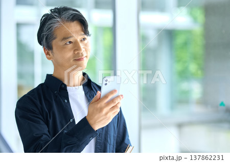 スマートフォンを手に持ち希望に満ちた表情で遠くを見つめるミドル世代の日本人男性 スマートフォンを手に持ち希望に満ちた表情で遠くを見つめるミドル世代の日本人男性 137862231