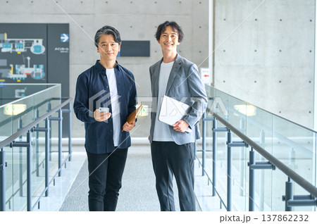 モダンなオフィスでノートパソコンとスマホを持つ笑顔のビジネスマン二人 モダンなオフィスでノートパソコンとスマホを持つ笑顔のビジネスマン二人 137862232