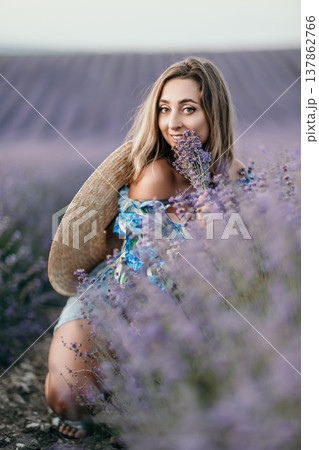 Lavender woman portrait of a beautiful young blonde female holding flowers and wearing a straw hat in a blooming field Lavender woman portrait of a beautiful young blonde female holding flowers and wearing a straw hat in a blooming field 137862766