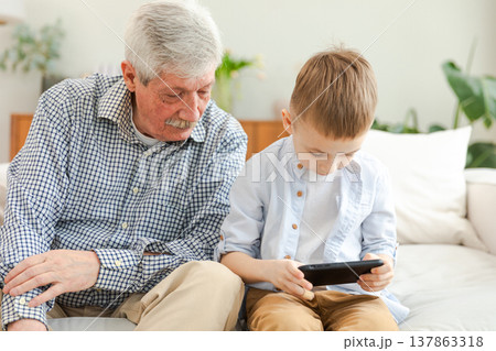 Happy family at home. Old senior man grandfather boy grandson enjoying time together watching video on phone. Good time at home. grandparent and child together. Older generation modern tech usage 137863318