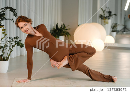Woman performs yoga pose in a studio with indoor plants and lighting at a morning class Woman performs yoga pose in a studio with indoor plants and lighting at a morning class 137863971