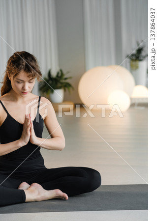 Woman practices yoga in a bright indoor space during morning hours while sitting in a cross-legged position with hands in prayer gesture Woman practices yoga in a bright indoor space during morning hours while sitting in a cross-legged position with hands in prayer gesture 137864037