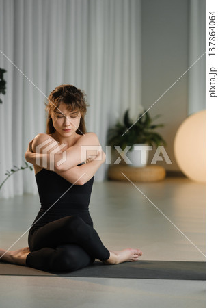 Woman practices yoga indoors while sitting on a mat in a well-lit studio with plants and soft lighting during a morning session Woman practices yoga indoors while sitting on a mat in a well-lit studio with plants and soft lighting during a morning session 137864064