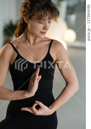 Woman practices yoga in a studio with plants and soft lighting during the day Woman practices yoga in a studio with plants and soft lighting during the day 137864086