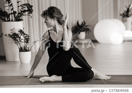 Woman practices yoga in a modern studio with plants and soft lighting during a daytime session focused on flexibility and relaxation 137864098