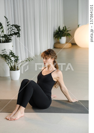 Woman practices yoga in a bright indoor space with plants and soft lighting during a morning session for health and wellness 137864101