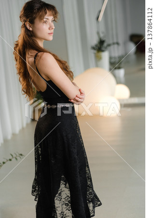 Woman poses in black dress at modern indoor venue with soft lighting during an event in the evening hours 137864112