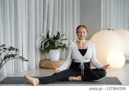 Yoga session at home with a woman practicing in a quiet room during daylight near plants and soft lighting 137864280