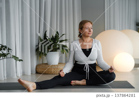 Yoga session at home with a woman practicing in a quiet room during daylight near plants and soft lighting Yoga session at home with a woman practicing in a quiet room during daylight near plants and soft lighting 137864281