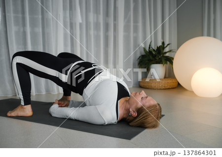 Woman practices yoga in a bright indoor space during morning hours with natural light streaming through sheer curtains Woman practices yoga in a bright indoor space during morning hours with natural light streaming through sheer curtains 137864301