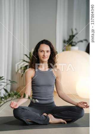 Woman practices yoga in a studio with plants and round lights during a morning session focused on mindfulness and relaxation 137864340