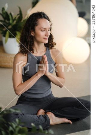 Woman practices yoga in a studio with soft lighting and plants during a morning session focused on mindfulness and relaxation Woman practices yoga in a studio with soft lighting and plants during a morning session focused on mindfulness and relaxation 137864342