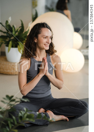 Woman practices yoga in a studio with plants and round lights during a morning session focused on mindfulness and relaxation Woman practices yoga in a studio with plants and round lights during a morning session focused on mindfulness and relaxation 137864345