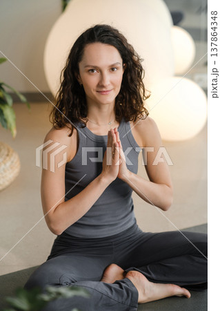 Woman practices yoga in a studio with plants and round lights during a morning session focused on mindfulness and relaxation 137864348