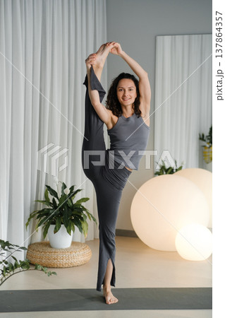 Yoga practice in a bright studio with a woman performing a balanced pose in comfortable clothing during a morning session Yoga practice in a bright studio with a woman performing a balanced pose in comfortable clothing during a morning session 137864357