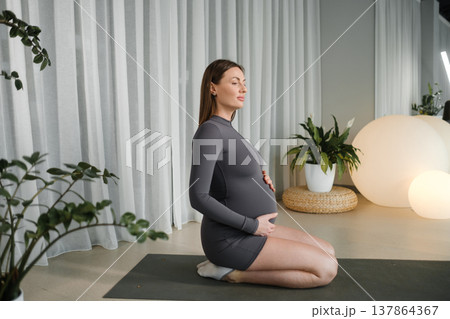 Pregnant woman practicing yoga in a calm indoor space with plants and soft lighting during evening hours 137864367