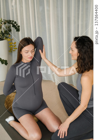 Two women practice yoga together in a bright indoor space with soft lighting in the morning, focusing on connection and support during pregnancy Two women practice yoga together in a bright indoor space with soft lighting in the morning, focusing on connection and support during pregnancy 137864400