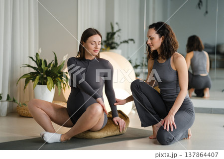 Two women practicing yoga together in a bright room with plants, mats, and soft lighting during a wellness session in the morning Two women practicing yoga together in a bright room with plants, mats, and soft lighting during a wellness session in the morning 137864407