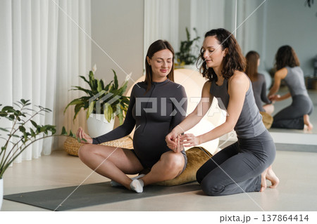 Pregnant woman practicing yoga with instructor in studio during day time with large plants and soft lighting around them Pregnant woman practicing yoga with instructor in studio during day time with large plants and soft lighting around them 137864414