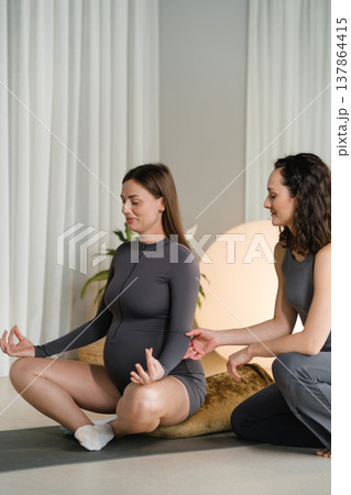 Pregnant woman practicing yoga with instructor in studio during day time with large plants and soft lighting around them Pregnant woman practicing yoga with instructor in studio during day time with large plants and soft lighting around them 137864415