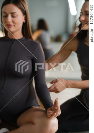 Yoga session for pregnant women in a studio setting with an instructor guiding a participant during a calm practice 137864419