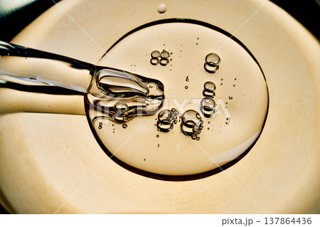 Pipette dripping golden serum with bubbles on surface 137864436