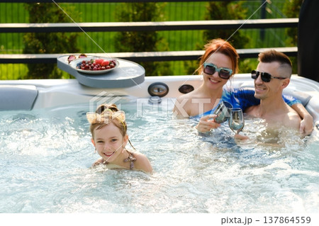 Family enjoys time together in hot tub while girl plays and parents relax on sunny day in backyard Family enjoys time together in hot tub while girl plays and parents relax on sunny day in backyard 137864559