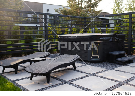 Hot tub area with lounge chairs in a backyard setting on a sunny day in a residential neighborhood surrounded by trees and a fence 137864615